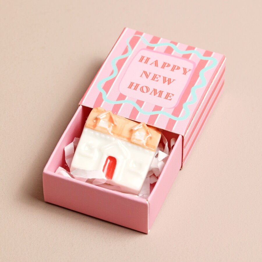 A Tiny Ceramic House Ornament Inside a Pink Matchbox Reading Happy New Home