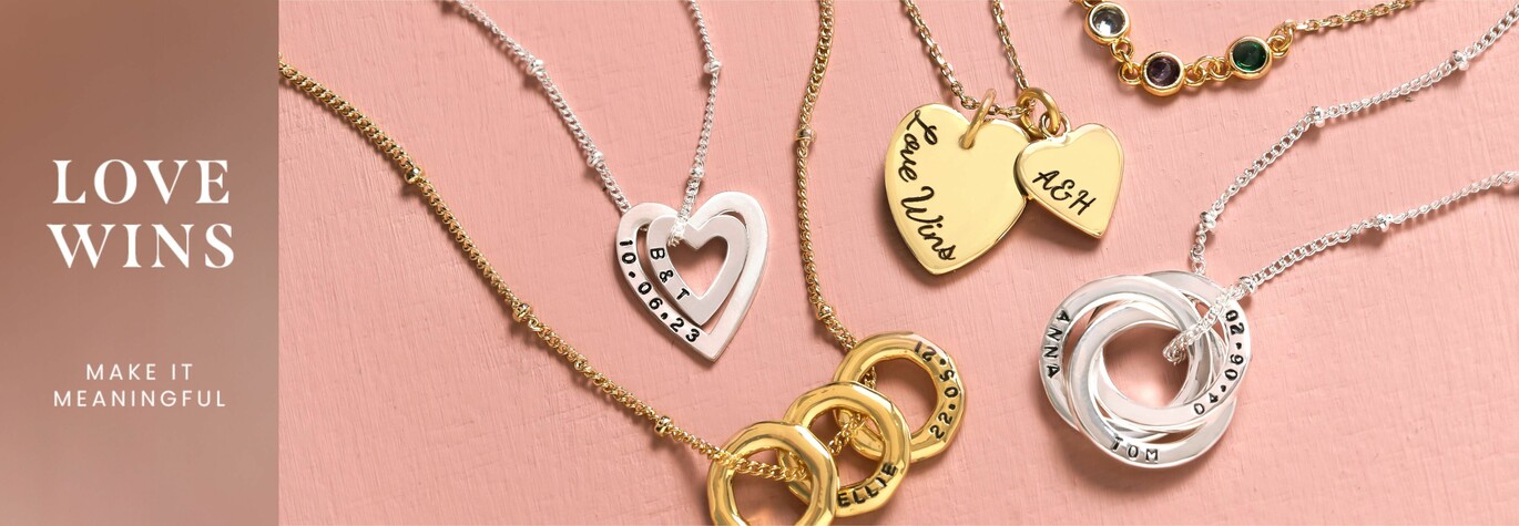 Selection of personalised jewellery pieces on a pink surface with love wins and make it meaningful on a banner to the left