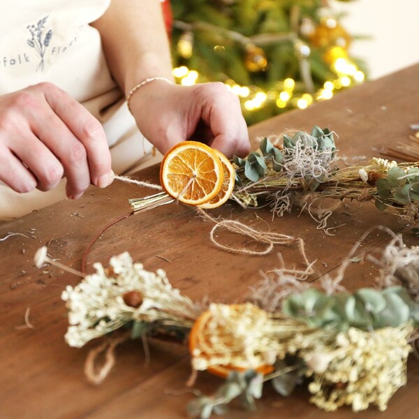Model finishing off tying branches and orange slices onto the wreath base