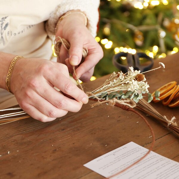 Model tying branches onto the wreath base of Gingerbread Christmas Dried Flower Wreath Kit