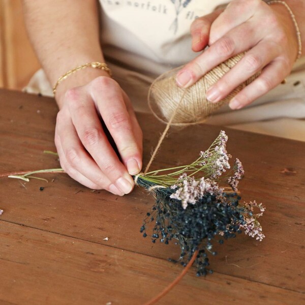 Model tying bunches of flowers from Luxury Midwinter Dried Flower Bouquet onto wreath base