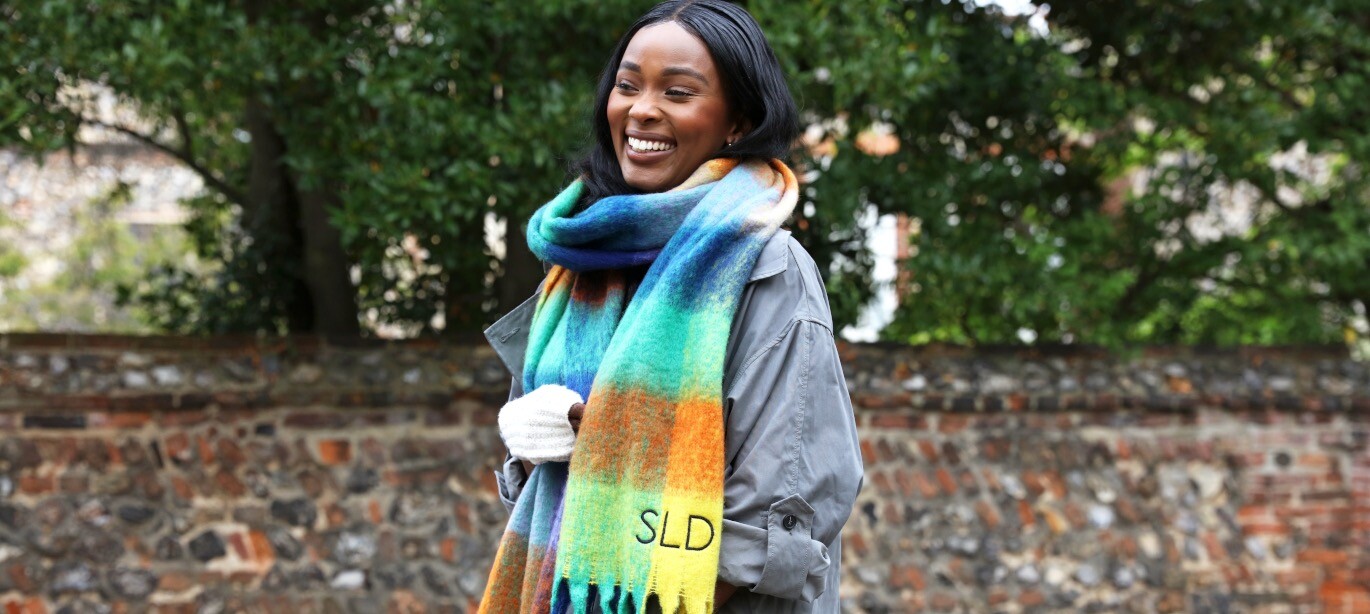 model wearing bright personalised scarf in front of stone wall and trees