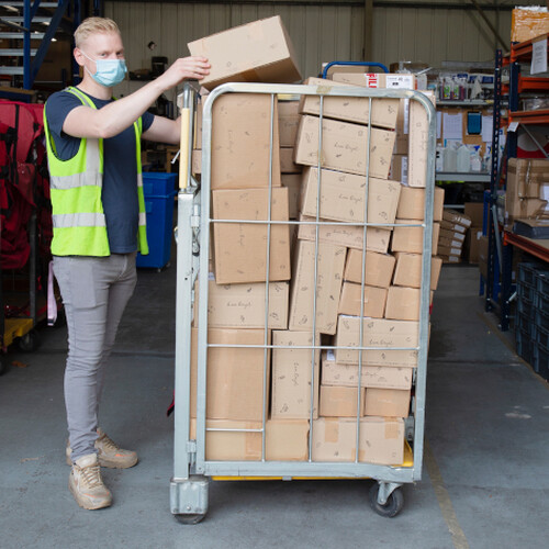 warehouse supervisor adding boxes to a stack of boxes on a trolley