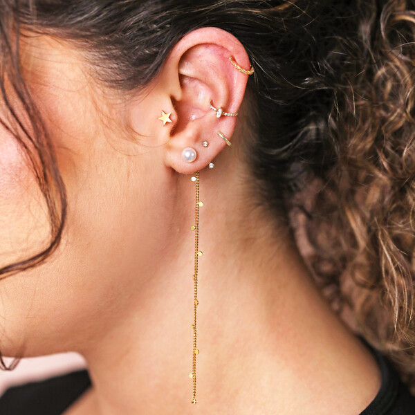 Model wearing pearl and chain drop earing, tiny swarovski jacket earrings and tiny gold huggie hoop in lobe piercing, marquise crystal earring in conch, gold star barbell in tragus and a twisted rope ear cuff on upper ear