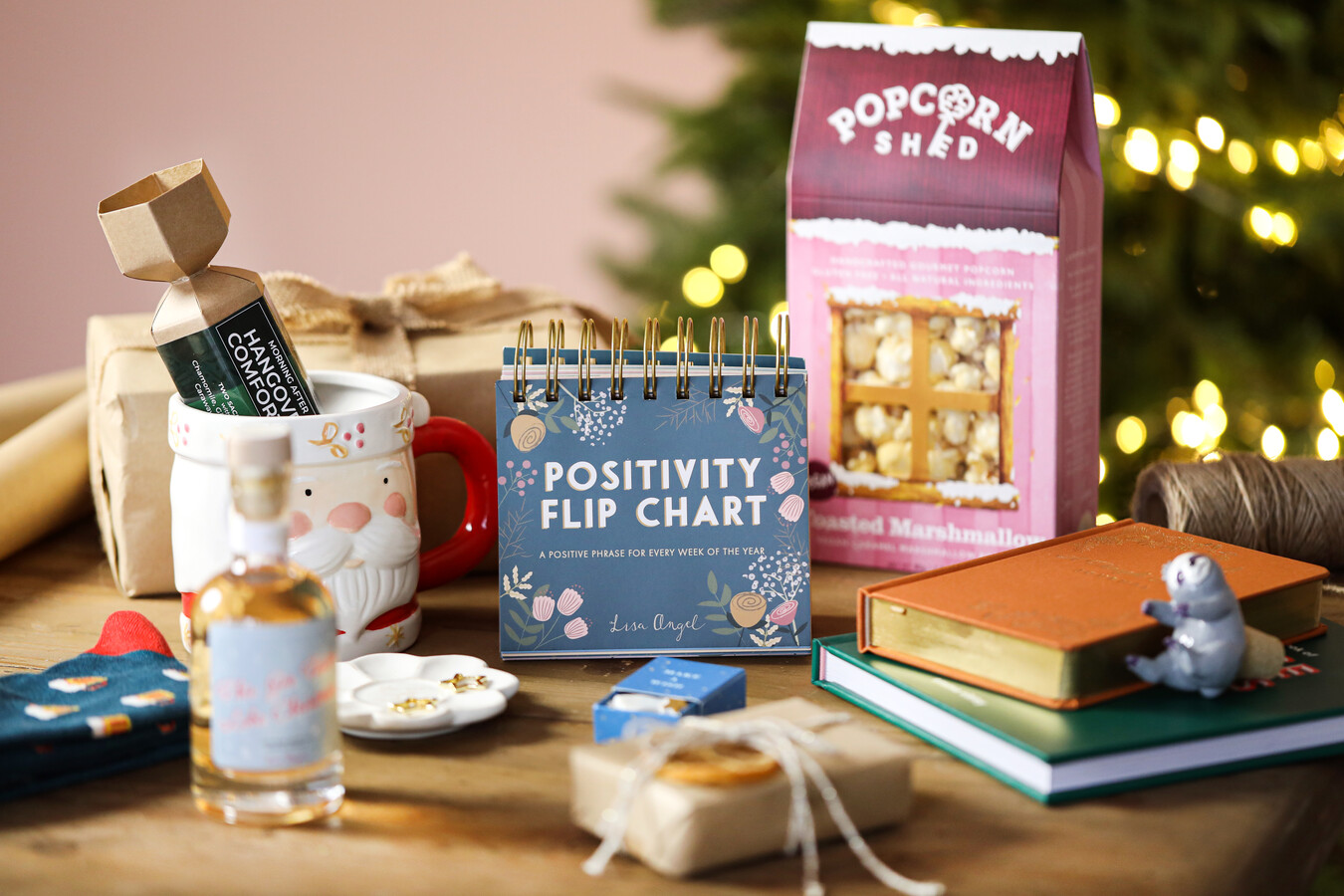 Top 15 Secret Santa gifts laid out on wooden table with lit Christmas tree in background