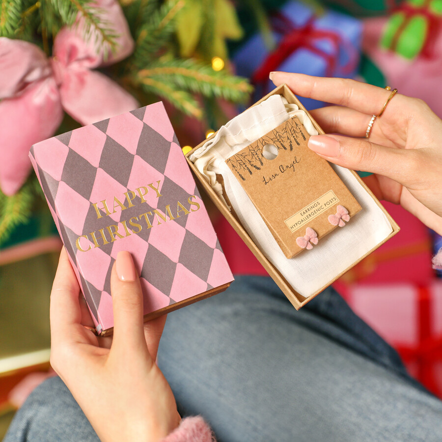 A Pair of Pink Velvet Bow-Shaped Earrings in a Patterned Gift Box Being Opened by Someone Next to the Christmas Tree
