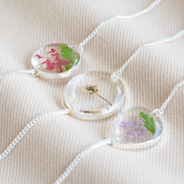 Pressed Birth Flower Charm Bracelet in Silver Three Silver Pressed Flower Charm Bracelets With Different Coloured Flowers on Neutral Fabric