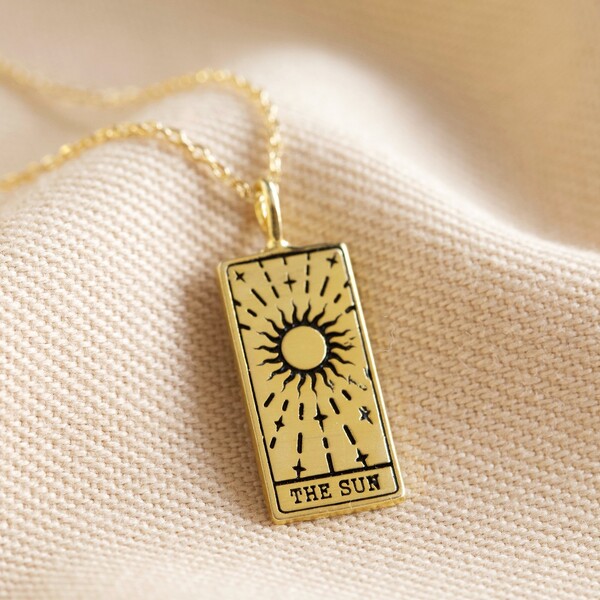 Gold the sun tarot card pendant necklace on top of beige coloured material