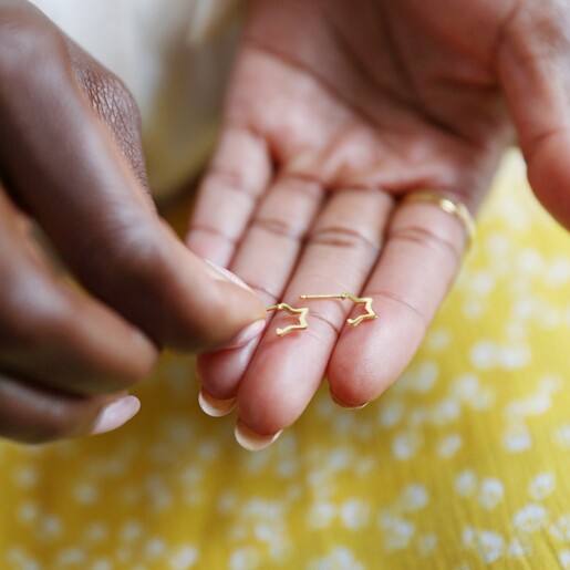 Model Holds Mini Gold Sterling Silver Star Huggie Hoop Earrings