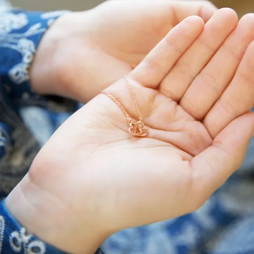 Hand Holding Ladies' Delicate Tiny Interlocking Hearts Necklace in Rose Gold
