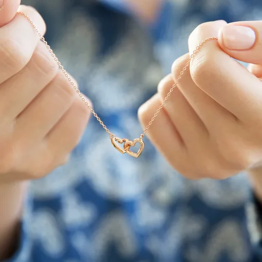 Hands Holding Ladies' Tiny Interlocking Hearts Necklace in Rose Gold