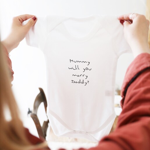 Model Holding Up Lisa Angel Personalised Proposal Short Sleeved Babygrow
