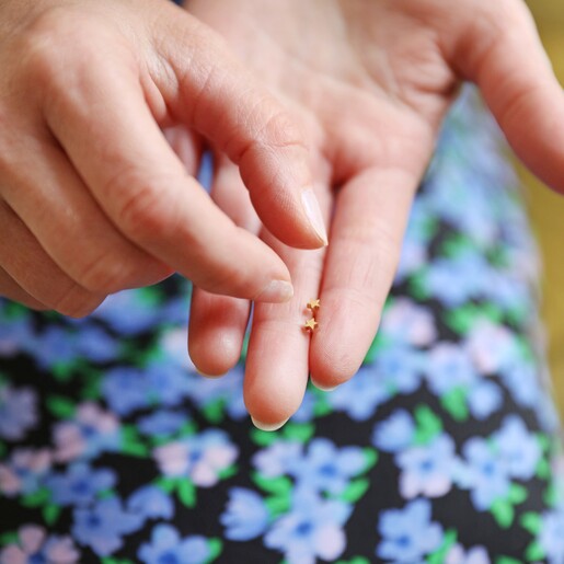 Model Holding Tiny Stainless Steel Star Stud Earrings in Gold