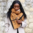Model Wearing Personalised Embroidered Check Blanket Scarf in Light Brown  with one hand on scarf and looking down