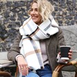 Model Wearing White and Beige Plaid Blanket Scarf looking to the side and holding a cup