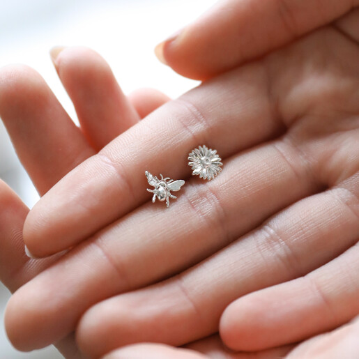 Model Holding Mismatched Daisy and Bee Stud Earrings in Silver in Between Fingers