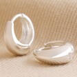 Close Up of Wide Domed Huggie Hoops in Silver on Neutral Fabric