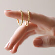 Textured Hoop Earrings in Gold on Model's Finger with Neutral Background