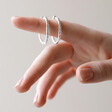 Model Holding Textured Hoop Earrings in Silver on Finger with Neutral Background