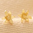 May Lily Tiny Birth Flower Stud Earrings in Gold on Neutral Fabric