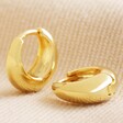 Wide Domed Huggie Hoop Earrings in Gold Upright with One Laid on Cream Fabric