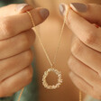 Model Holding Floral Halo Pendant Necklace in Gold in Front with Necklace Hanging Between Hands