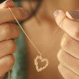 Model Holding Floral Heart Pendant Necklace in Gold with Pendant Hanging Between Hands