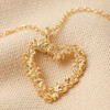 Close Up of Pendant on Floral Heart Pendant Necklace in Gold on Beige Fabric