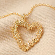 Close Up of Pendant on Floral Heart Pendant Necklace in Gold on Beige Fabric