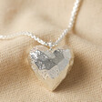Close Up of Large 3D Molten Heart Pendant Necklace in Silver on Beige Fabric