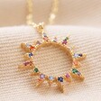 Close Up of Pendant on Rainbow Crystal Sunburst Pendant Necklace in Gold on Beige Fabric
