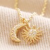 Close Up of Sun and Moon Charm Necklace in Gold on Beige Fabric