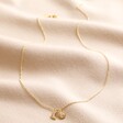 Sun and Moon Charm Necklace in Gold Full Length Stretched on Beige Coloured Fabric