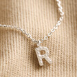 Close Up of R Initial Pendant from Tiny Pearl Initial Charm Necklace in Silver on Beige Fabric