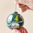 Hand-Painted Norwich Snow Globe Bauble Held by Model in front of Neutral Background