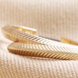 Close Up of Herringbone Edge Hoop Earrings in Gold Laid on Natural Fabric