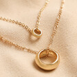 Close Up of Layered Ring Pendant Necklace in Gold on Cream Background