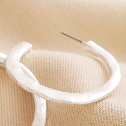 Close Up of Organic Hammered Hoop Earrings in Silver on Natural Coloured Fabric