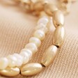 Close Up of Pearl and Matte Bead Layered Bracelet in Gold on Beige Coloured Fabric