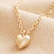 Close Up of Pendant on Tiny Heart Pendant Necklace in Gold on Beige Fabric