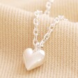 Close Up of Pendant on Tiny Heart Pendant Necklace in Silver on Natural Coloured Fabric