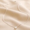 Tiny Heart Pendant Necklace in Silver Full Length on Beige Coloured Fabric