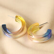 Big Metal London Iridescent Resin Hoop Earrings in Yellow and Blue on Neutral Fabric