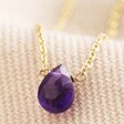 Close Up of Semi-Precious Amethyst Stone Teardrop Pendant Necklace in Gold on Beige Fabric