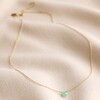 Semi-Precious Chrysoprase Stone Teardrop Pendant Necklace in Gold Laid Out on Rippled Beige Fabric