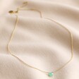 Semi-Precious Chrysoprase Stone Teardrop Pendant Necklace in Gold Laid Out on Rippled Beige Fabric