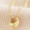 Close Up of Semi-Precious Citrine Stone Teardrop Pendant Necklace in Gold on Beige Fabric