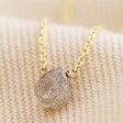 Close Up of Semi-Precious Grey Labradorite Stone Teardrop Pendant Necklace in Gold on Beige Fabric