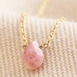 Close Up Semi-Precious Pink Thulite Stone Teardrop Pendant Necklace in Gold on Beige Fabric