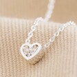 Close Up of Tiny Crystal Heart Pendant Necklace in Silver on Beige Fabric